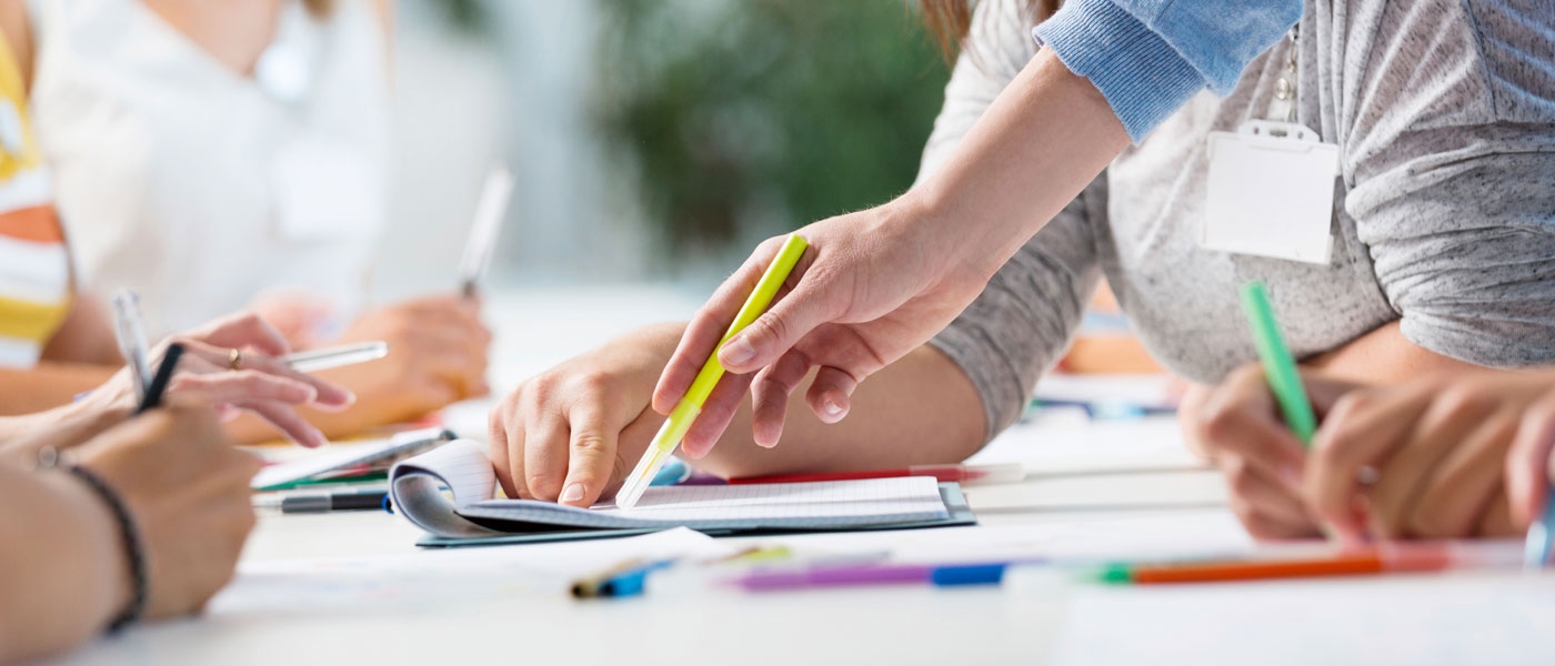 Photo of hands holding pens point at paper