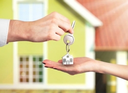 House keychain being handed over from one hand to another with a green house in the background